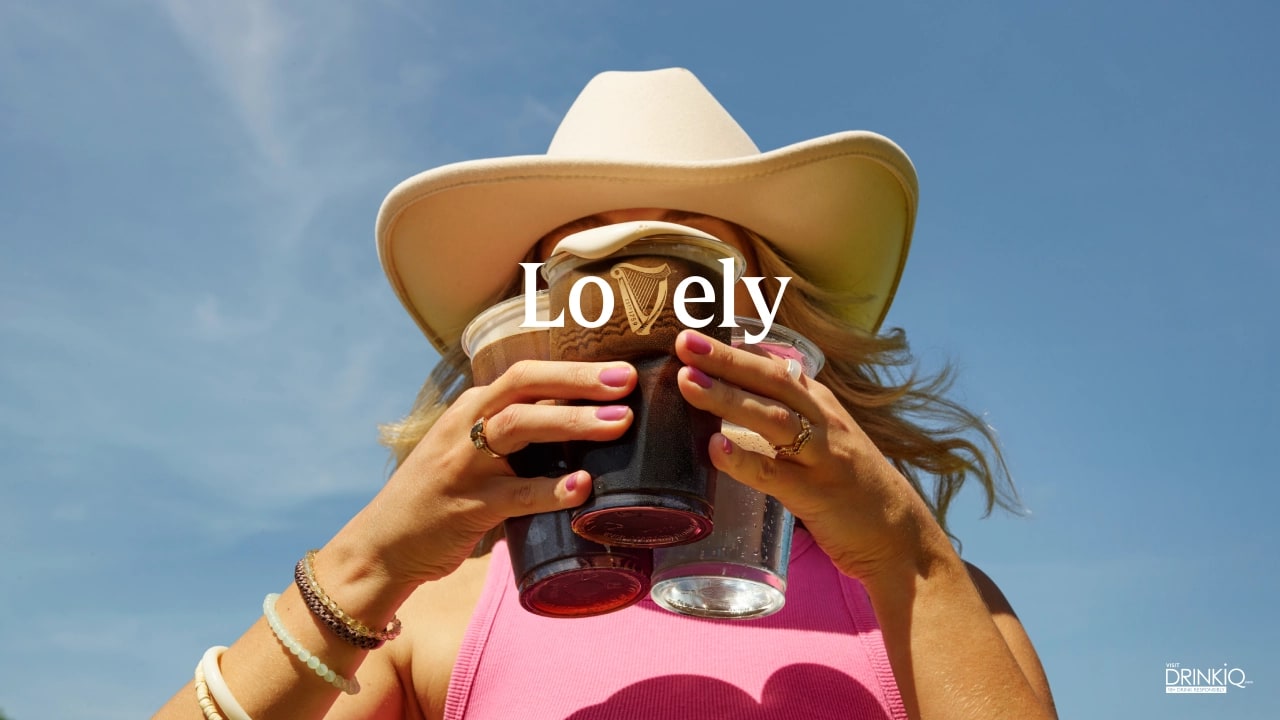 Woman in cowboy hat holds a Guinness 'Lovely' branded cup against blue sky